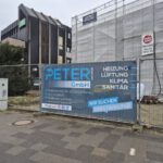 Eine Baustelle mit einem Banner der Firma Peter GmbH an einem Bauzaun