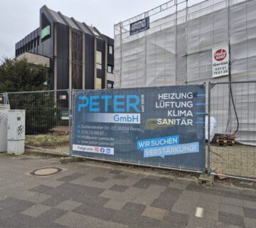 Eine Baustelle mit einem Banner der Firma Peter GmbH an einem Bauzaun
