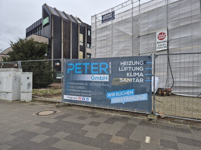 Eine Baustelle mit einem Banner der Firma Peter GmbH an einem Bauzaun